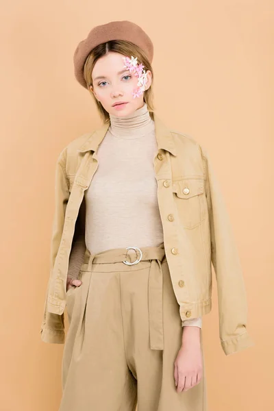 Mujer elegante con flores en la cara con boina y de pie aislado en beige - foto de stock