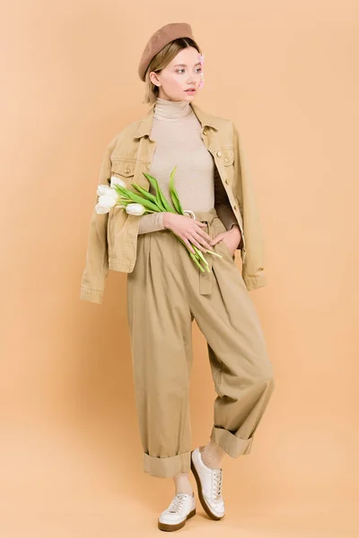 Mulher na moda vestindo boina e segurando buquê isolado no bege — Fotografia de Stock