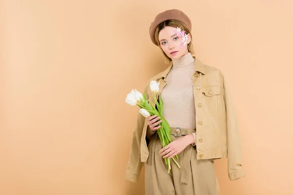 Attractive woman wearing beret and holding bouquet isolated on beige — Stock Photo