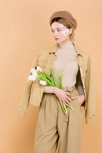 Attraktive Frau in Baskenmütze mit Blumenstrauß auf Beige — Stockfoto