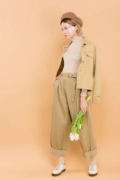 Stylish woman in beret holding bouquet of flowers isolated on beige — Stock Photo