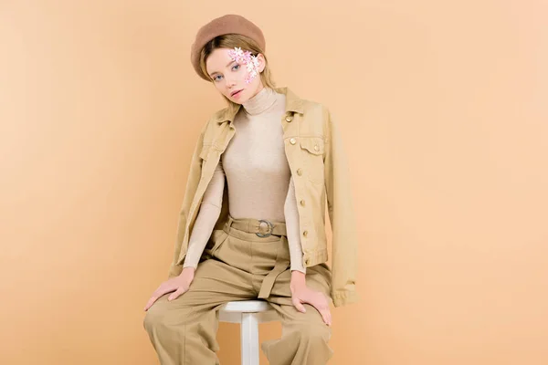 Femme à la mode dans béret assis sur chaise isolé sur beige — Photo de stock