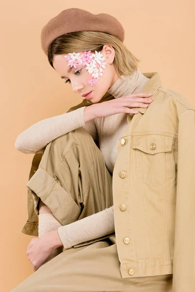 Trendige Frau mit Blumen im Gesicht trägt Baskenmütze isoliert auf beige — Stockfoto