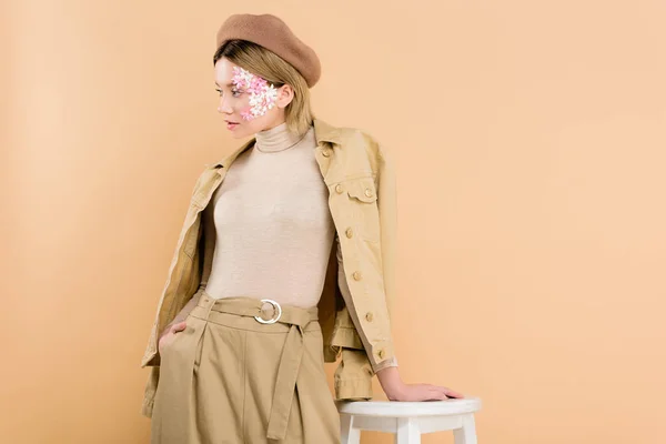 Stylische Frau in Baskenmütze steht neben Stuhl isoliert auf beige — Stockfoto