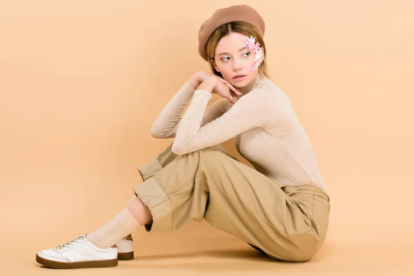 Belle fille en béret posant tout en étant assis sur le sol isolé sur beige — Photo de stock