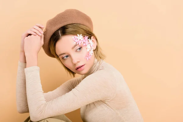 Attraente donna con fiori sul viso indossa berretto isolato su beige — Foto stock