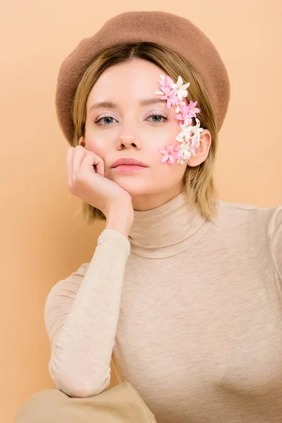 Femme sérieuse avec des fleurs sur le visage regardant caméra isolé sur beige — Photo de stock