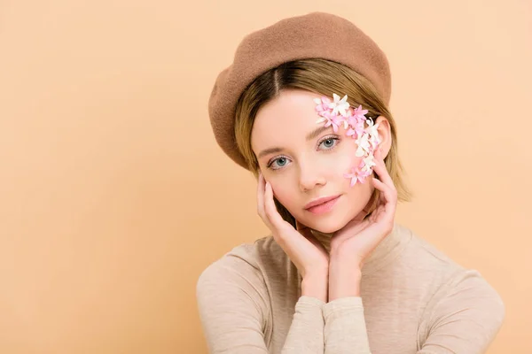 Schöne Frau mit Blumen im Gesicht trägt trendige Baskenmütze isoliert auf beige — Stockfoto
