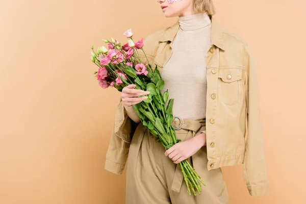 Vue recadrée femme élégante avec des fleurs sur le visage tenant bouquet isolé sur beige — Photo de stock