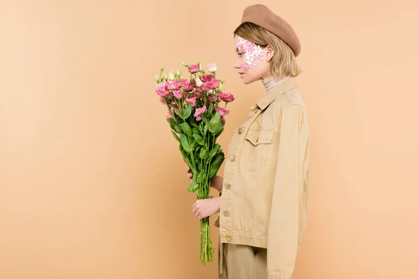 Profile of stylish woman with flowers on face holding bouquet isolated on beige — Stock Photo