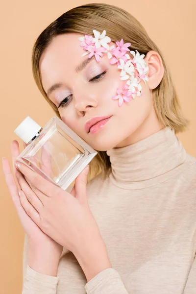 Atractiva mujer con flores en la cara sosteniendo botella de perfume aislado en beige - foto de stock