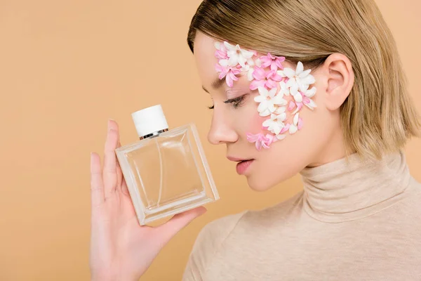 Attraktive Frau mit Blumen im Gesicht, die eine Flasche Parfüm isoliert auf Beige betrachtet — Stockfoto