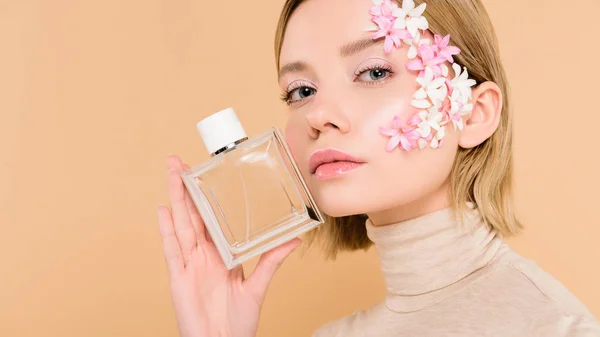 Selbstbewusste Frau mit Blumen im Gesicht, die eine Flasche Parfüm auf Beige hält — Stockfoto