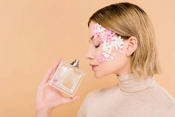 Beautiful woman with flowers on face smelling perfume isolated on beige — Stock Photo