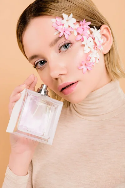 Jolie femme avec des fleurs sur le visage tenant bouteille de parfum à la main isolé sur beige — Photo de stock