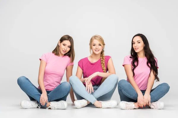 Happy girls sitting with crossed legs on floor on grey background — Stock Photo