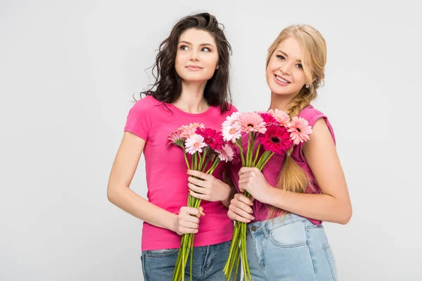 Счастливые девушки, держащие цветы и стоящие в одиночестве на сером — стоковое фото