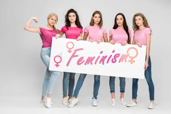 Ernsthafte Mädchen mit großem Schild mit Feminismus-Schriftzug auf grauem Hintergrund — Stockfoto