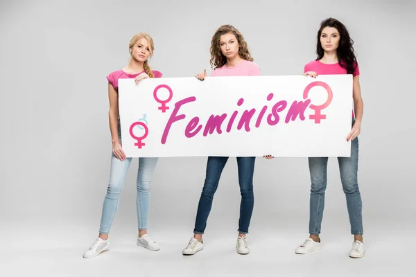 Впевнені дівчата, що тримають великий знак з фемінізмом на сірому фоні — стокове фото