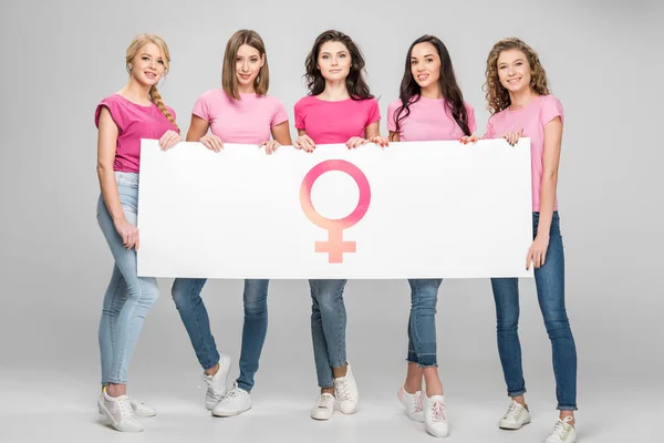 Chicas atractivas sosteniendo letrero grande con símbolo femenino sobre fondo gris - foto de stock