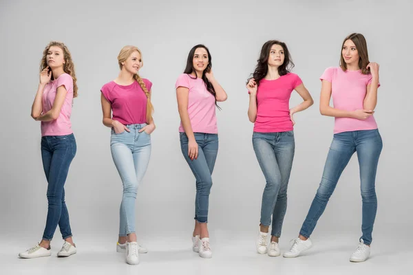 Beautiful girl standing with hands in pockets near attractive friends on grey background — Stock Photo