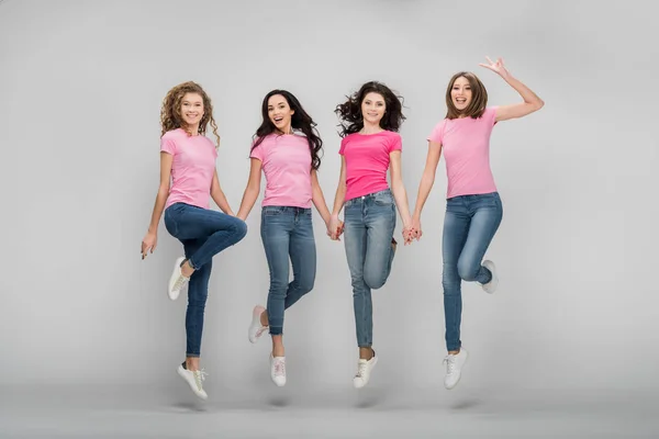 Cheerful girls holding hands and jumping on grey background — Stock Photo