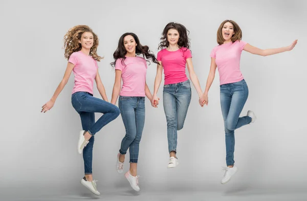 Happy girls holding hands and jumping on grey background — Stock Photo