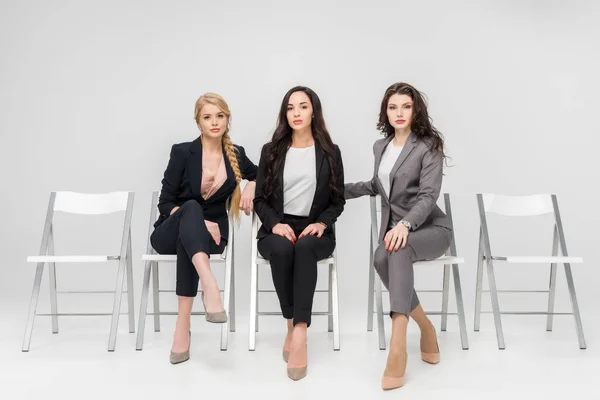 Attraente giovani donne in abito formale seduta con gambe incrociate isolato su grigio — Foto stock