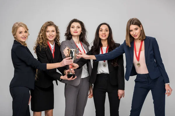 Exitosas empresarias sosteniendo trofeo sonriendo aisladas en gris - foto de stock