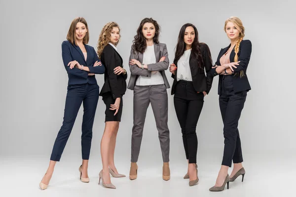 Mujeres jóvenes atractivas de pie con brazos cruzados sobre fondo gris - foto de stock