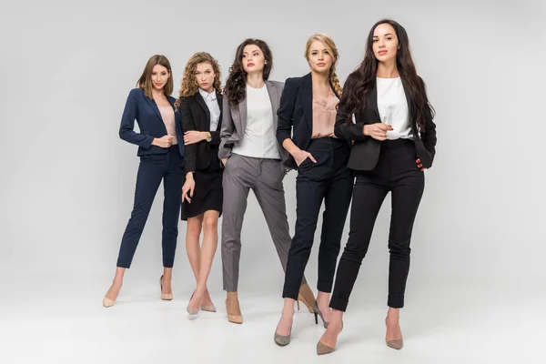 Belles jeunes femmes réussies debout avec les mains dans les poches sur fond gris — Photo de stock