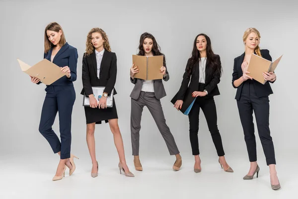 Schöne junge Geschäftsfrauen halten Klemmbretter und Ordner in der Hand, während sie auf grauem Hintergrund stehen — Stockfoto