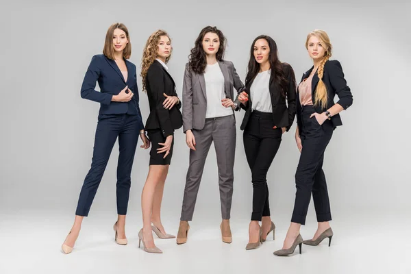 Hermosas mujeres exitosas de pie con las manos en los bolsillos sobre fondo gris - foto de stock