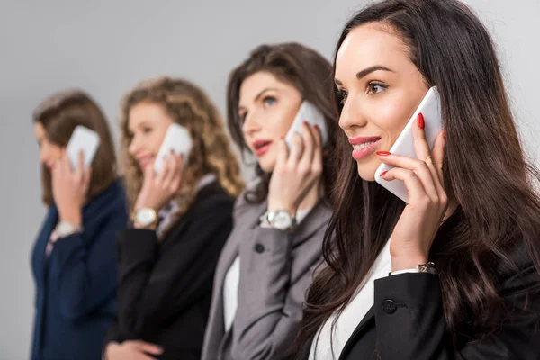 Enfoque selectivo de las mujeres alegres hablando en teléfonos inteligentes aislados en gris - foto de stock