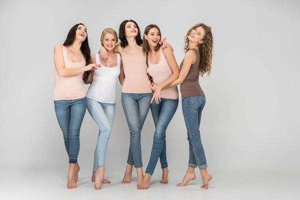 Happy young women hugging while standing together and laughing on grey background — Stock Photo