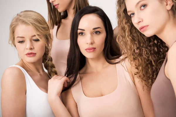 Mujeres atractivas de pie juntas mientras se apoyan aisladas en gris - foto de stock