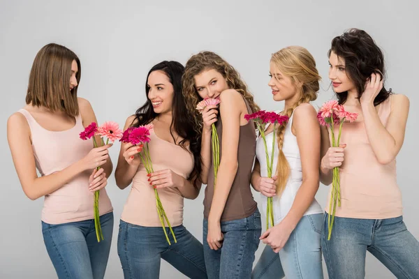 Нежные девушки, держащие розовые цветы и стоящие изолированные на сером — стоковое фото