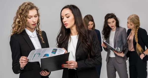Selective focus of attractive businesswoman looking at charts and graphs while holding clipboard near colleague with attractive coworkers on background — Stock Photo