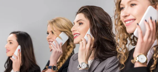 Enfoque selectivo de chicas alegres hablando en teléfonos inteligentes aislados en gris - foto de stock