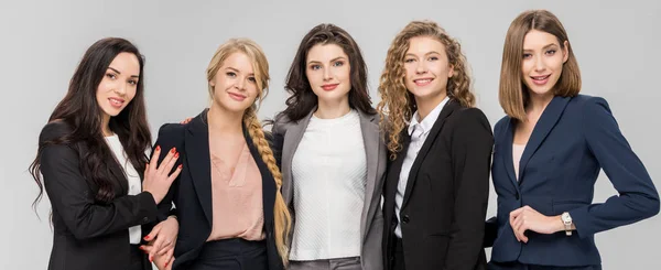 Hermosas mujeres jóvenes en ropa formal de pie y sonriendo aislado en gris - foto de stock