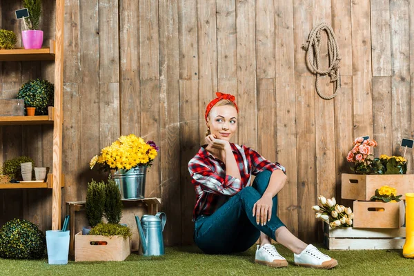 Thoughtful woman sitting with crossed legs on grass near wooden fence — Stock Photo