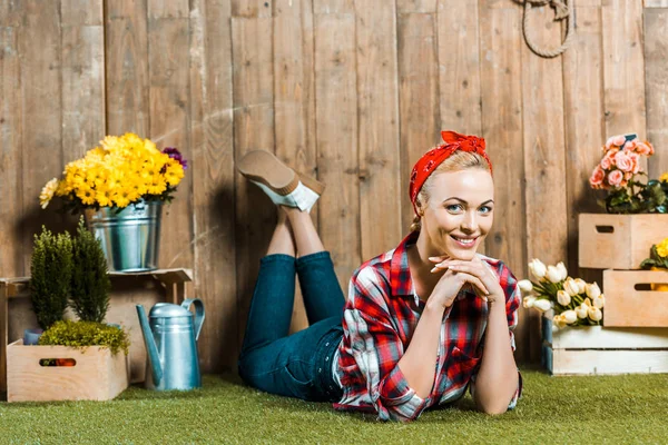 Glückliche Frau liegt mit überkreuzten Beinen auf Gras neben Holzzaun und Blumen — Stockfoto