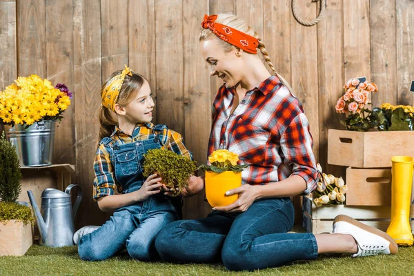 Daughter looking at cheerful mother and holding plant near wooden fence — Stock Photo