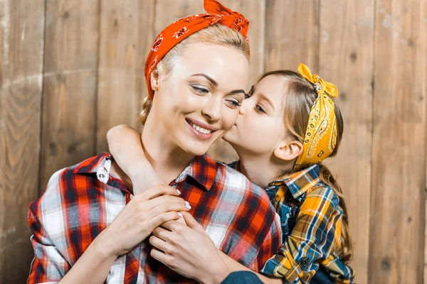 Cute daughter kissing cheek of happy mother near wooden fence — Stock Photo