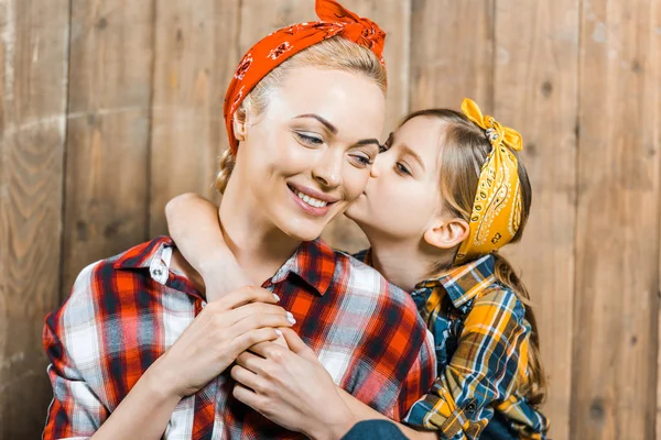 Mignonne fille baisers joue de mère heureuse près de clôture en bois — Photo de stock