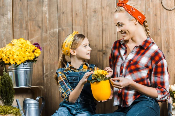 Daughter looking at cheerful mother while touching flowers near wooden fence — Stock Photo