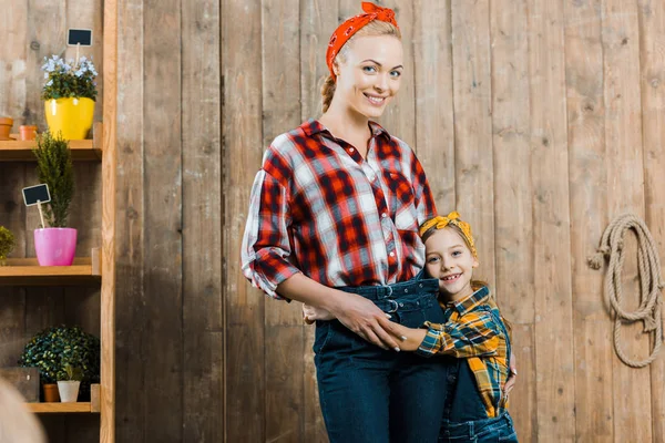 Niño feliz abrazando hermosa madre de pie cerca de valla - foto de stock