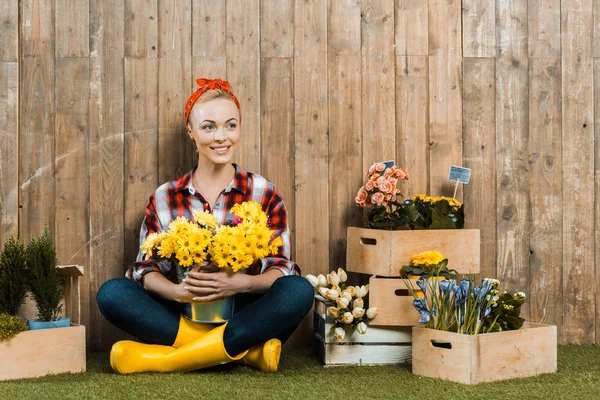 Mujer feliz sentada con las piernas cruzadas y sosteniendo flores - foto de stock