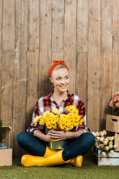 Smiling woman sitting with crossed legs and holding flowers in bucket — Stock Photo