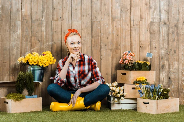 Beautiful woman sitting with crossed legs near flowers in wooden boxes — Stock Photo